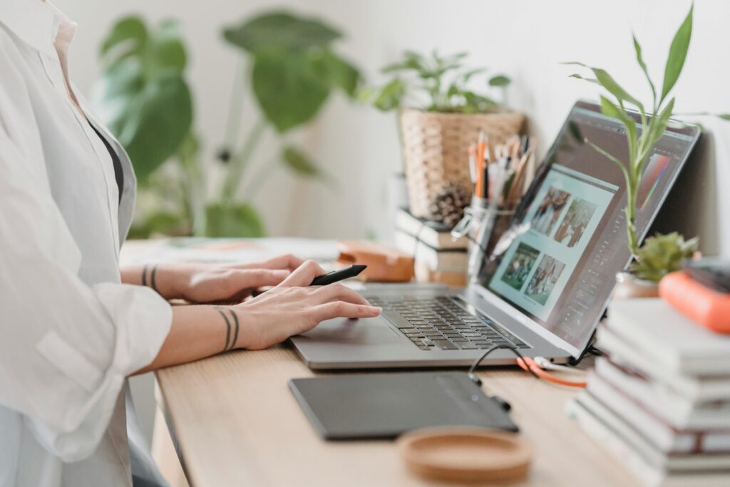 pexels-photo-7014337-7014337 Freelance designer working from home using a laptop and digital tablet, surrounded by plants.
