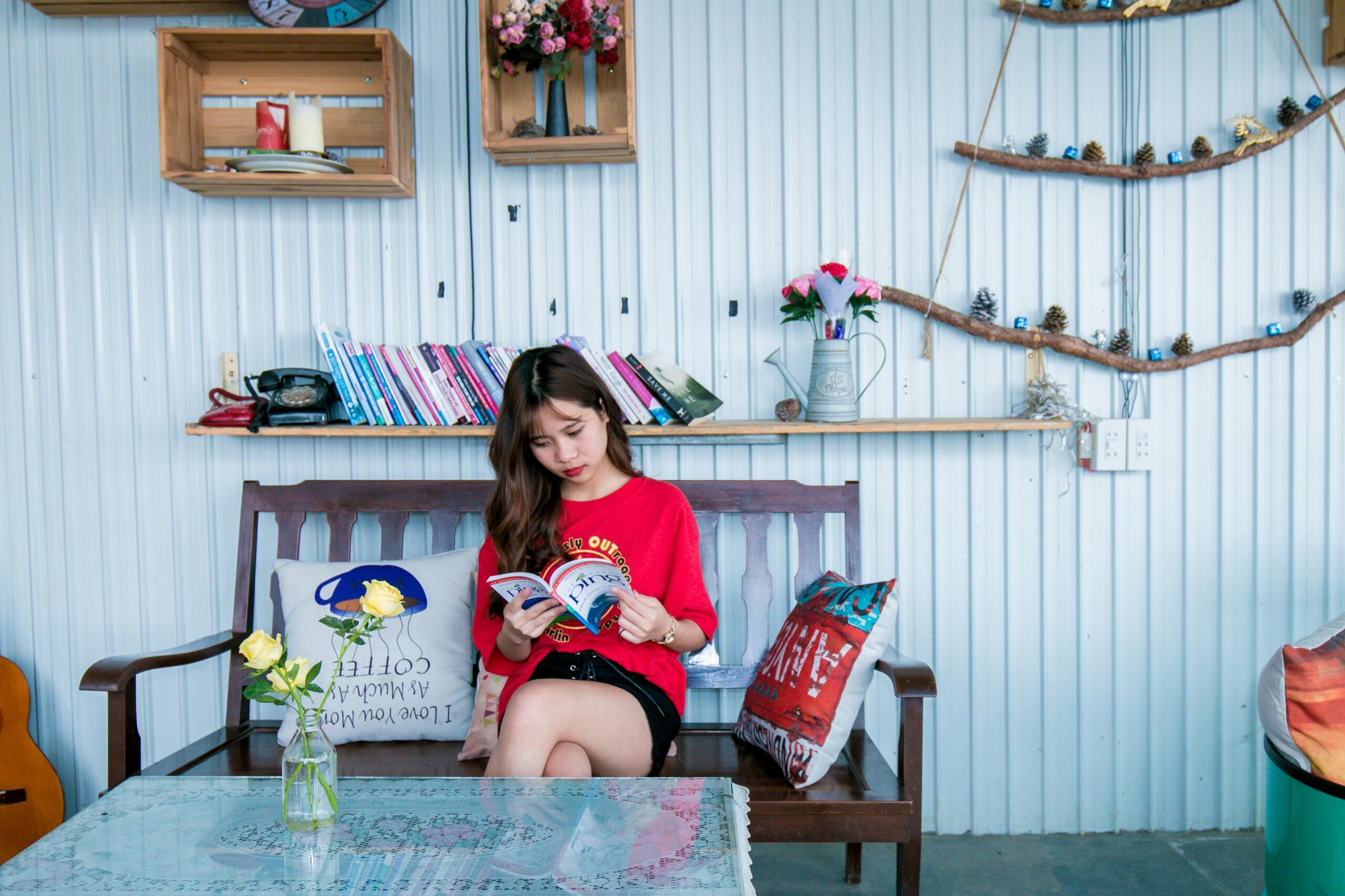 Young Asian woman relaxing indoors while reading a book. Cozy, colorful room for leisure.