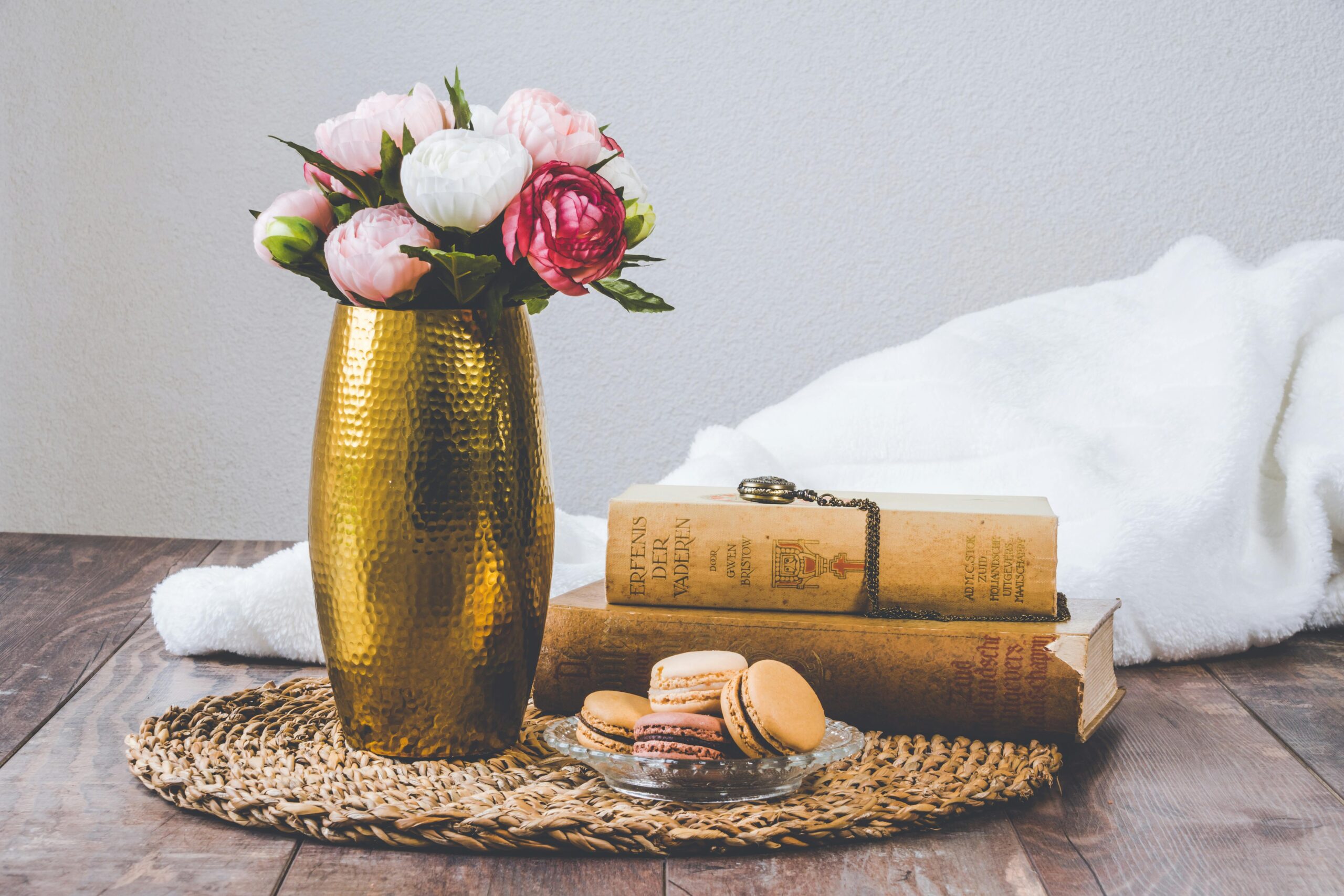 A rustic still life composition with macarons, vintage books, and a flower vase on wooden table.