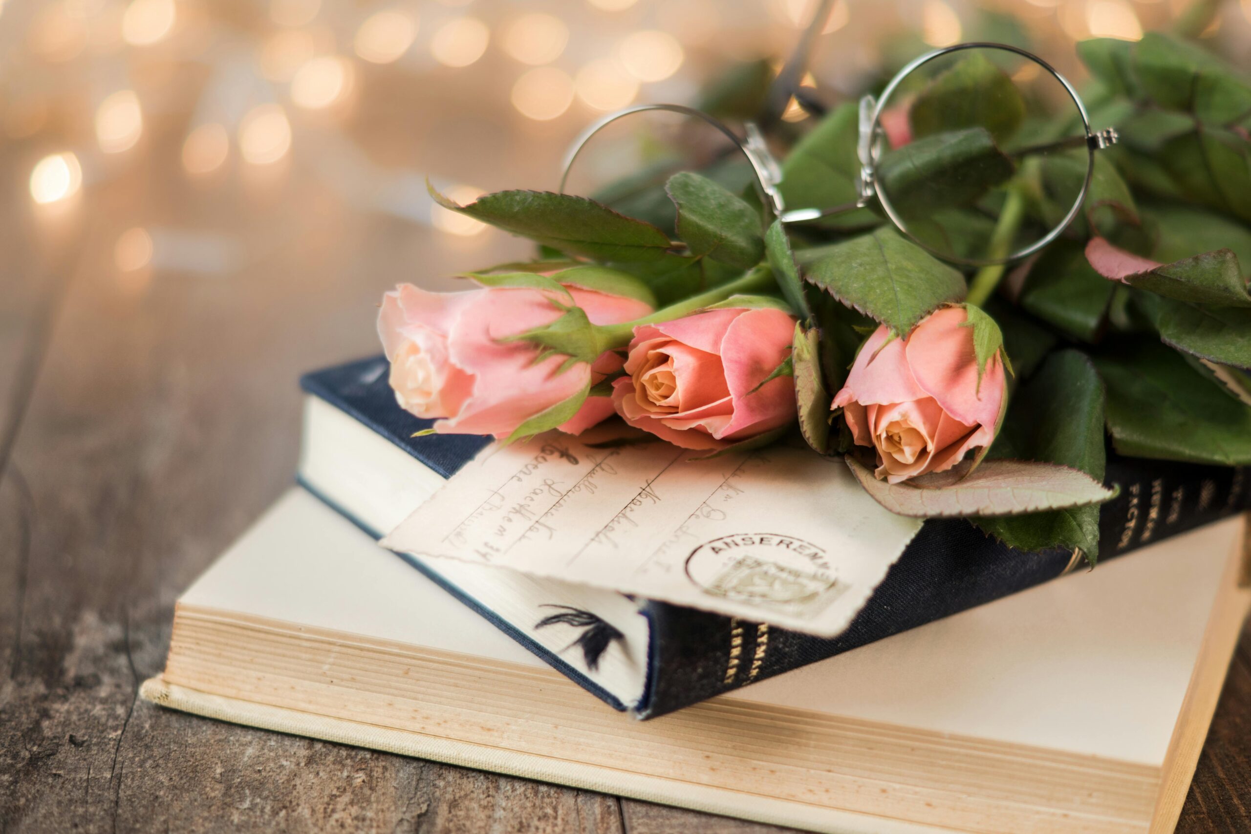 Elegant arrangement of pink roses on vintage books with glasses, perfect for romantic occasions.