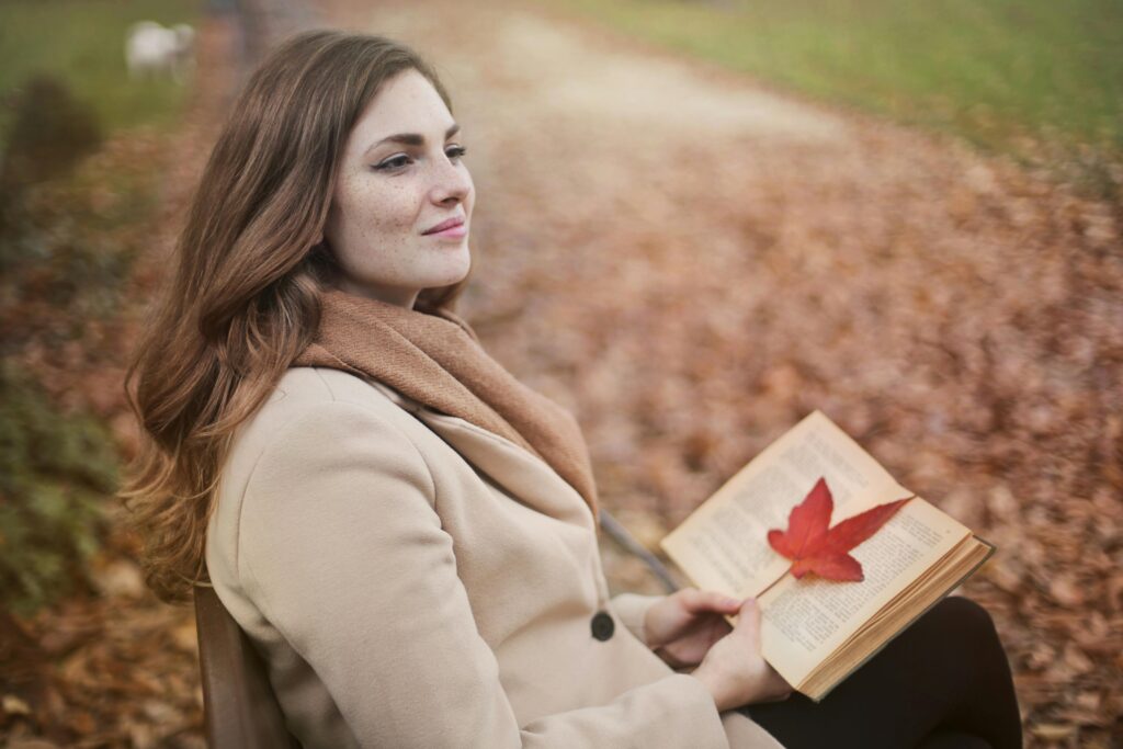 pexels-photo-3769732-3769732 Side view of peaceful young female in warm coat and scarf sitting on bench with open book in hands and looking away pensively while resting in autumn park