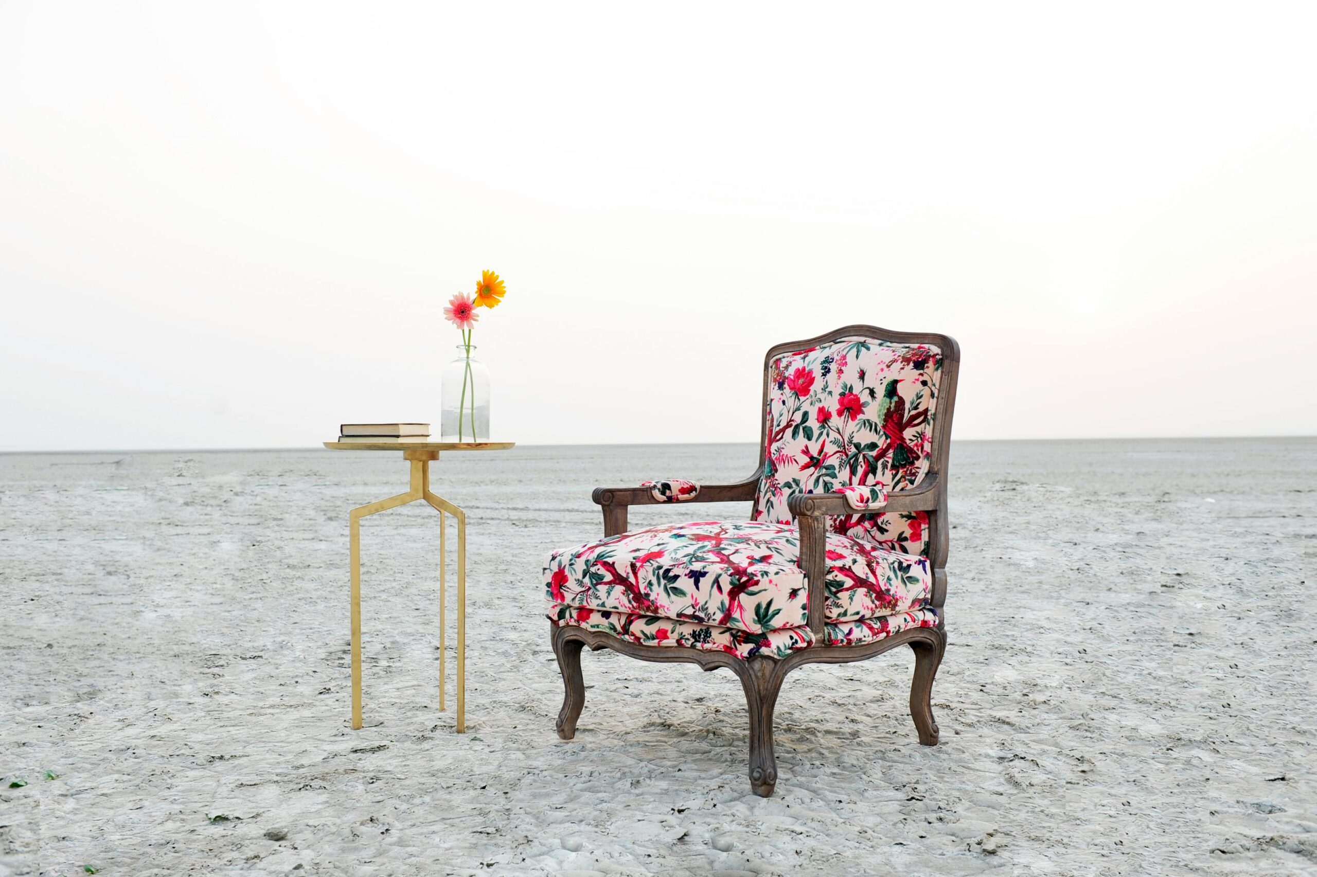 A floral armchair and vase on a table create a striking contrast against the barren desert backdrop.