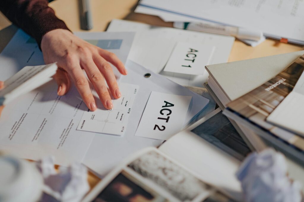 pexels-photo-8086362-8086362 A cluttered desk with scripts, notes, and a person's hand organizing screenplay drafts.
